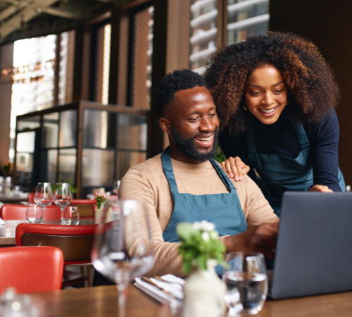 man and woman business owners in cafe using laptop