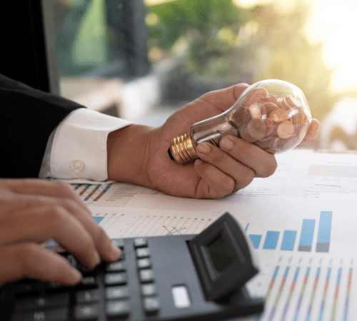 Man holding light bulb with coins in whilst using calculator