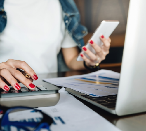 Woman on laptop and phone with spreadsheets and calculator