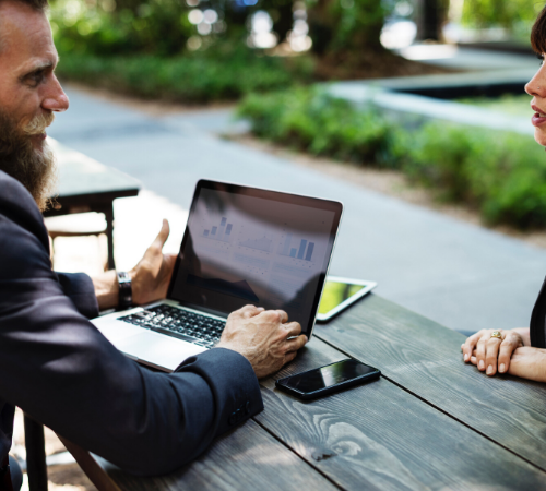 Business man and woman outside on bench with laptop 
